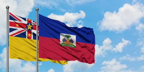 Bandera de Niue y Haití ondeando en el viento contra el cielo azul nublado blanco juntos. Concepto diplomático, relaciones internacionales . — Foto de Stock