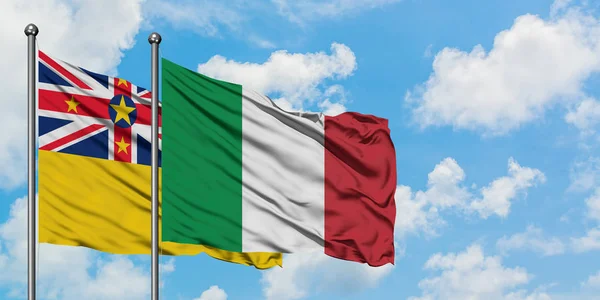 Bandera de Niue e Italia ondeando en el viento contra el cielo azul nublado blanco juntos. Concepto diplomático, relaciones internacionales . — Foto de Stock