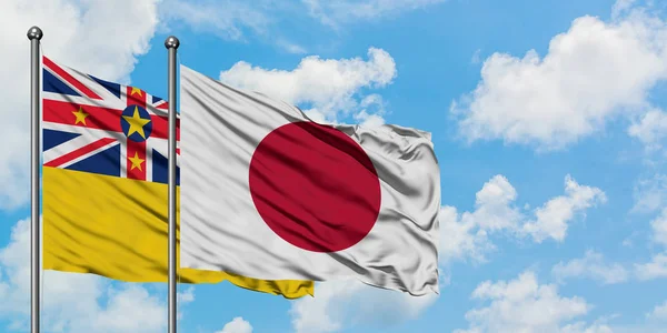 Bandera de Niue y Japón ondeando en el viento contra el cielo azul nublado blanco juntos. Concepto diplomático, relaciones internacionales . —  Fotos de Stock