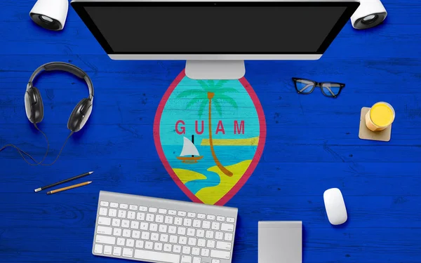 Guam flag background with headphone,computer keyboard and mouse on national office desk table.Top view with copy space.Flat Lay.