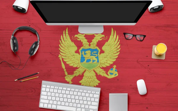 Montenegro flag background with headphone,computer keyboard and mouse on national office desk table.Top view with copy space.Flat Lay.