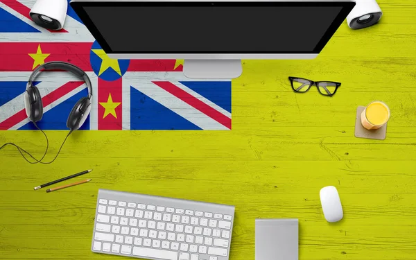 Niue flag background with headphone,computer keyboard and mouse on national office desk table.Top view with copy space.Flat Lay.