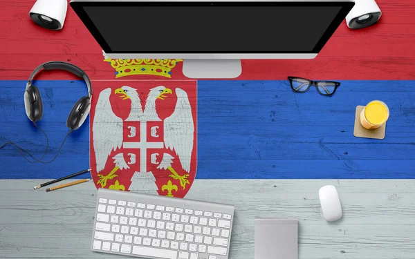 Serbia flag background with headphone,computer keyboard and mouse on national office desk table.Top view with copy space.Flat Lay.