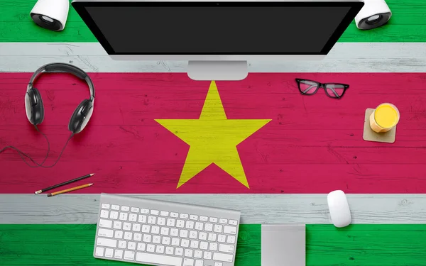 Suriname flag background with headphone,computer keyboard and mouse on national office desk table.Top view with copy space.Flat Lay.