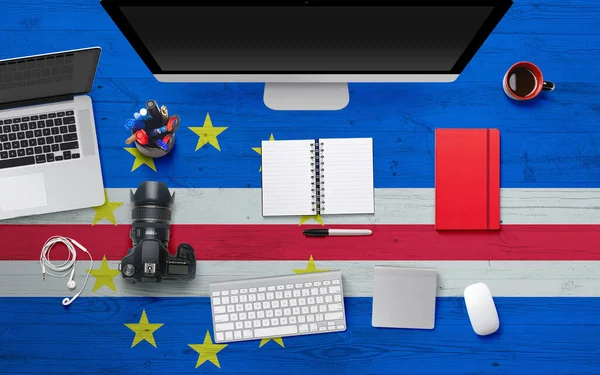 Cape Verde flag background with headphone,camera, notebook and mouse on national office desk table.Top view with copy space.Flat Lay.