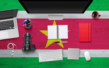 Suriname flag background with headphone,camera, notebook and mouse on national office desk table.Top view with copy space.Flat Lay. clipart