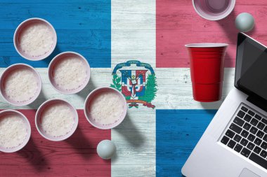 Dominik Cumhuriyeti bayrağı konsepti plastik bira bardakları ve laptop ulusal ahşap masa, üst manzara. Bira pong oyunu.