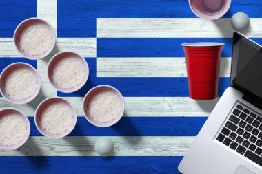 Yunanistan, ulusal ahşap masa üzerinde plastik bira bardakları ve dizüstü bilgisayarlı bayrak konsepti, üst manzara. Bira pong oyunu.