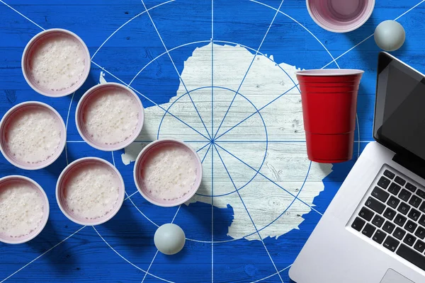 Antarctica flag concept with plastic beer pong cups and laptop on national wooden table, top view. Beer Pong game.