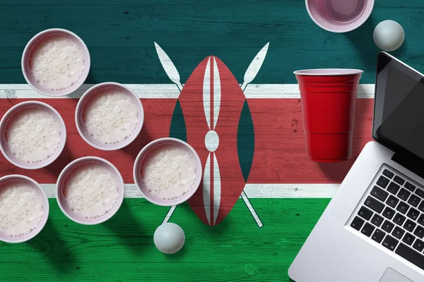 Kenya flag concept with plastic beer pong cups and laptop on national wooden table, top view. Beer Pong game.