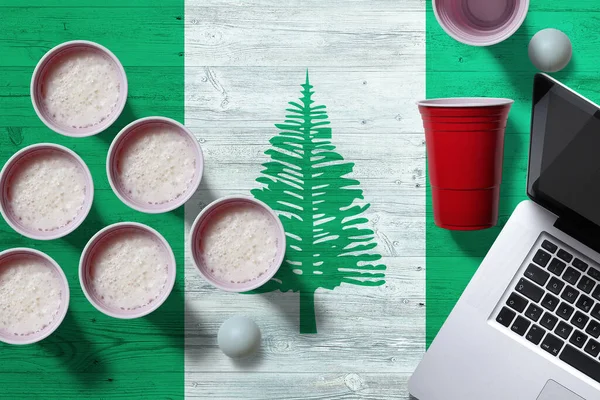 Norfolk Island flag concept with plastic beer pong cups and laptop on national wooden table, top view. Beer Pong game.