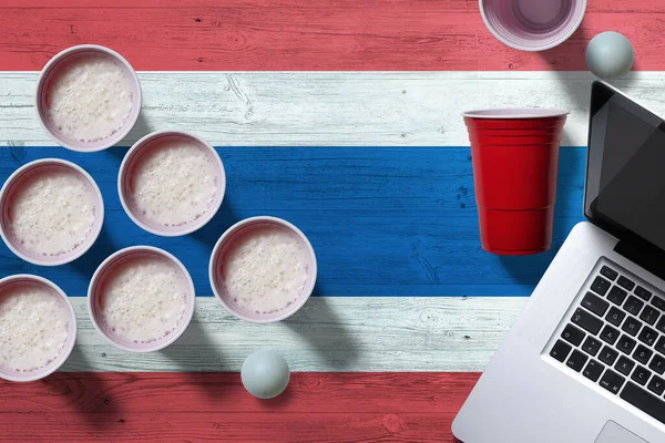 Thailand flag concept with plastic beer pong cups and laptop on national wooden table, top view. Beer Pong game.