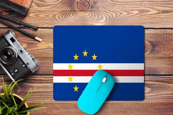 Cape Verde flag on wooden background with blue wireless mouse on a mouse pad, top view. Digital media concept.