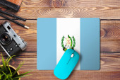 Guatemala vlajka na dřevěném pozadí s modrou bezdrátovou myší na podložce myši, horní pohled. Koncept digitálních médií.