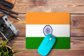 Indie vlajka na dřevěném pozadí s modrou bezdrátovou myší na podložce myši, pohled shora. Koncept digitálních médií.