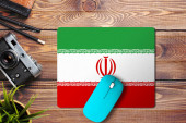 Íránská vlajka na dřevěném pozadí s modrou bezdrátovou myší na podložce myši, pohled shora. Koncept digitálních médií.