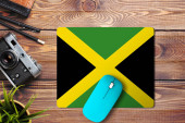 Jamajka vlajka na dřevěném pozadí s modrou bezdrátovou myší na podložce myši, horní pohled. Koncept digitálních médií.
