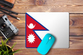Nepál vlajka na dřevěném pozadí s modrou bezdrátovou myší na podložce myši, pohled shora. Koncept digitálních médií.
