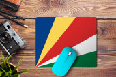 Seychely vlajka na dřevěném pozadí s modrou bezdrátovou myší na podložce myši, horní pohled. Koncept digitálních médií.