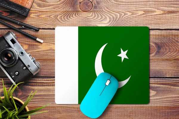Pakistan flag on wooden background with blue wireless mouse on a mouse pad, top view. Digital media concept.