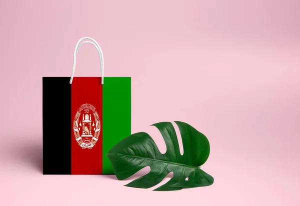 Afghanistan shopping concept. National cardboard shopping bag with monstera leaf and pink background. Online shopping theme.