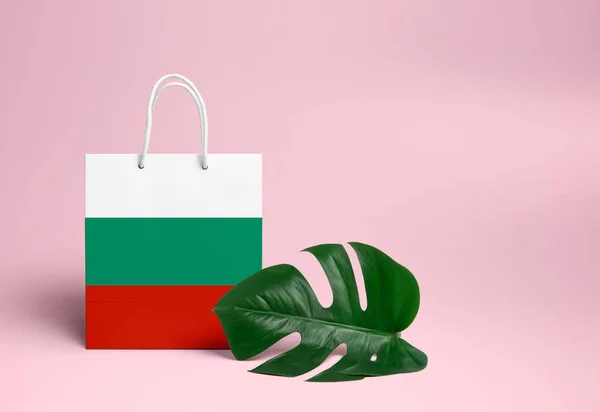 Bulgaria shopping concept. National cardboard shopping bag with monstera leaf and pink background. Online shopping theme.