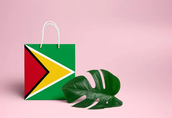 Guyana shopping concept. National cardboard shopping bag with monstera leaf and pink background. Online shopping theme.