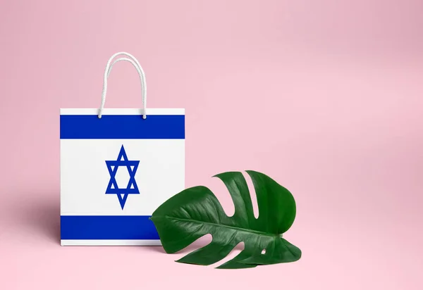 Israel shopping concept. National cardboard shopping bag with monstera leaf and pink background. Online shopping theme.