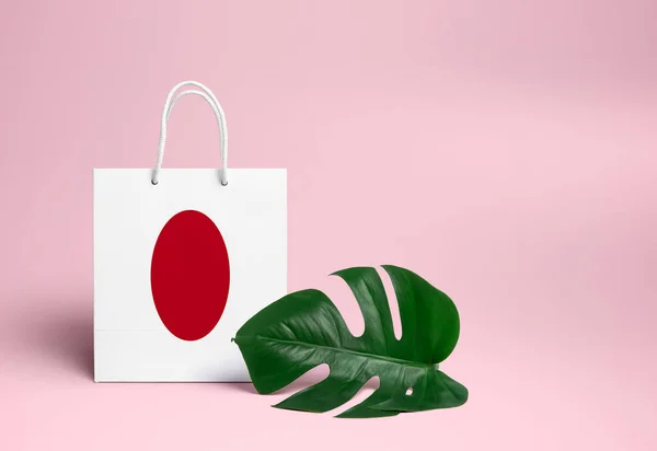 Japan shopping concept. National cardboard shopping bag with monstera leaf and pink background. Online shopping theme.
