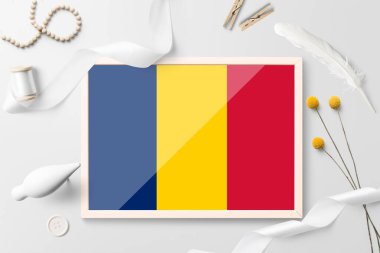 Beyaz yaratıcı arka planda ahşap çerçeveli Chad bayrağı. Beyaz tema, tüy, papatya, düğme, kurdele nesneleri.