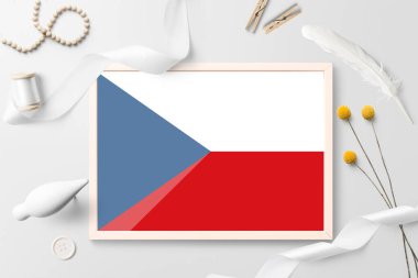 Beyaz yaratıcı arka planda tahta çerçeveli Çek Cumhuriyeti bayrağı. Beyaz tema, tüy, papatya, düğme, kurdele nesneleri.