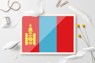 Beyaz yaratıcı arka planda ahşap çerçeveli Moğolistan bayrağı. Beyaz tema, tüy, papatya, düğme, kurdele nesneleri.