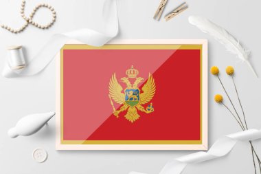 Karadağ beyaz yaratıcı arka planda ahşap çerçevede bayrak sallıyor. Beyaz tema, tüy, papatya, düğme, kurdele nesneleri.