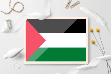 Beyaz yaratıcı arka planda tahta çerçeveli Filistin bayrağı. Beyaz tema, tüy, papatya, düğme, kurdele nesneleri.