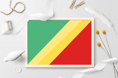 Kongo Cumhuriyeti bayrağı beyaz yaratıcı arka planda ahşap çerçevede. Beyaz tema, tüy, papatya, düğme, kurdele nesneleri.