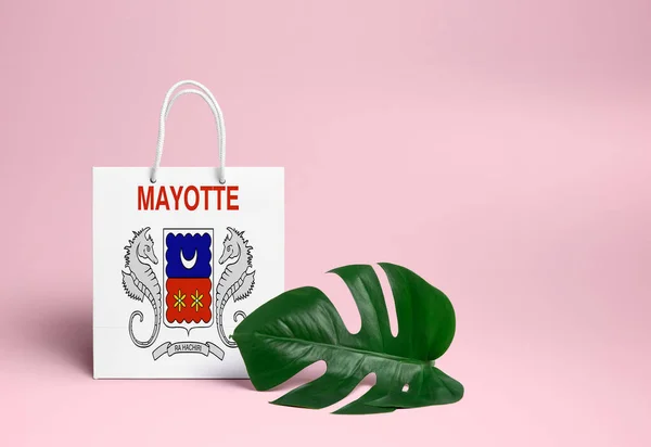 Mayotte shopping concept. National cardboard shopping bag with monstera leaf and pink background. Online shopping theme.