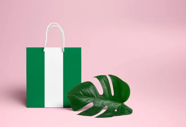 Nigeria shopping concept. National cardboard shopping bag with monstera leaf and pink background. Online shopping theme.