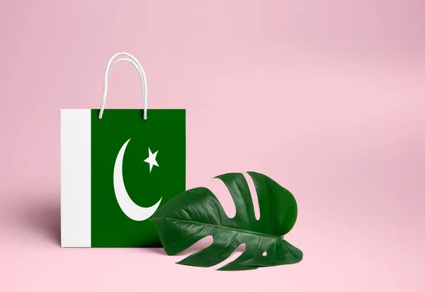 Pakistan shopping concept. National cardboard shopping bag with monstera leaf and pink background. Online shopping theme.