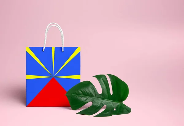 Reunion shopping concept. National cardboard shopping bag with monstera leaf and pink background. Online shopping theme.
