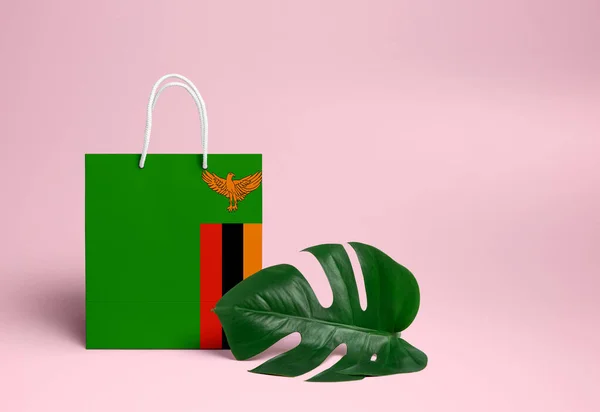 Zambia shopping concept. National cardboard shopping bag with monstera leaf and pink background. Online shopping theme.
