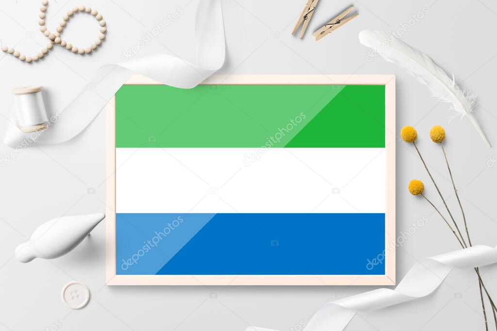 Sierra Leone flag in wooden frame on white creative background. White theme, feather, daisy, button, ribbon objects.