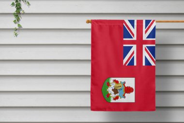 Bermuda national small flag hangs from a picket fence along the wooden wall in a rural town. Independence day concept. clipart