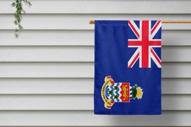 Cayman Islands national small flag hangs from a picket fence along the wooden wall in a rural town. Independence day concept. clipart