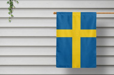 Sweden national small flag hangs from a picket fence along the wooden wall in a rural town. Independence day concept. clipart