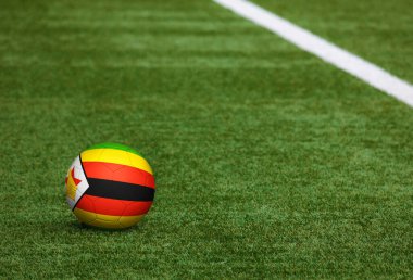 Futbol sahasında top üzerinde Zimbabwe bayrağı. Ulusal futbol teması yeşil çimlerde. Spor yarışması konsepti.