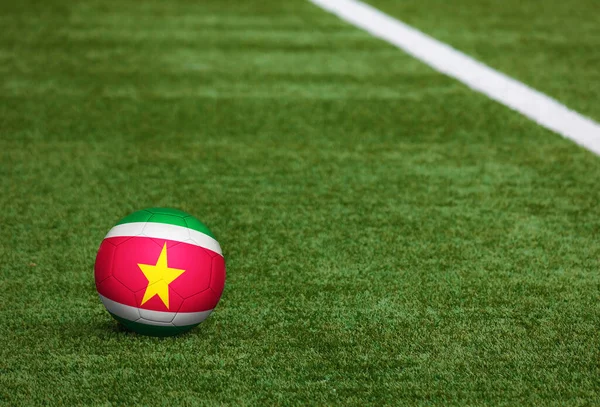 Suriname flag on ball at soccer field background. National football theme on green grass. Sports competition concept.