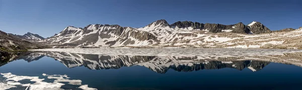 A panoramic reflection of snowy mountains reflecting on a frozen Wanda Lake, Evolution Basin, Kings Canyon National Park, California.