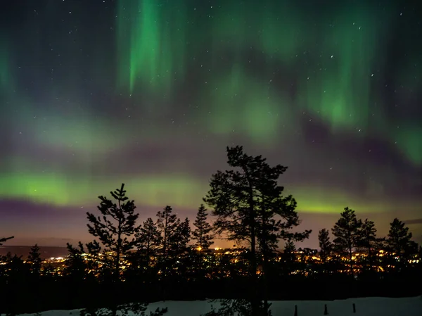 Kuzey ışıkları ve Rovaniemi Finlandiya 'da arka planda şehir ışıkları
