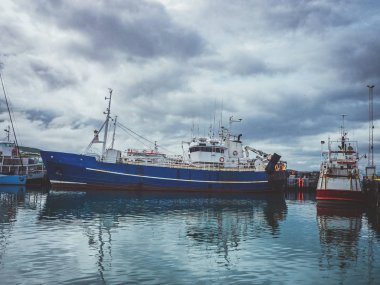 Husavik, İzlanda - 27 Temmuz 2016: Husavik limanında bulutlu gökyüzü ile mavi balıkçı gemisi ve deniz suyuna yansıması
