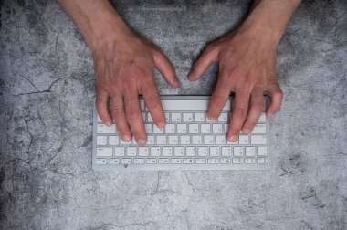 Koyu gri arka planda elleri olan klavye. Asfalt beton duvar kağıdı. Bağlam, yazar, programcı, ofis çalışmaları.